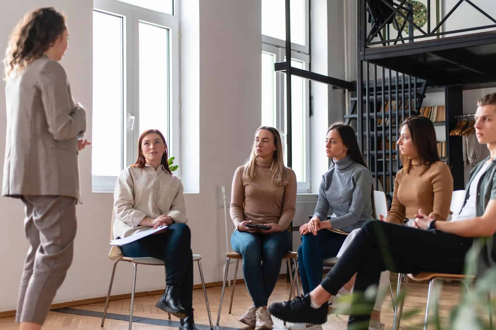 Facilitator leading a small group therapy or coaching session in a modern, well-lit space focused on mental wellness and emotional growth.