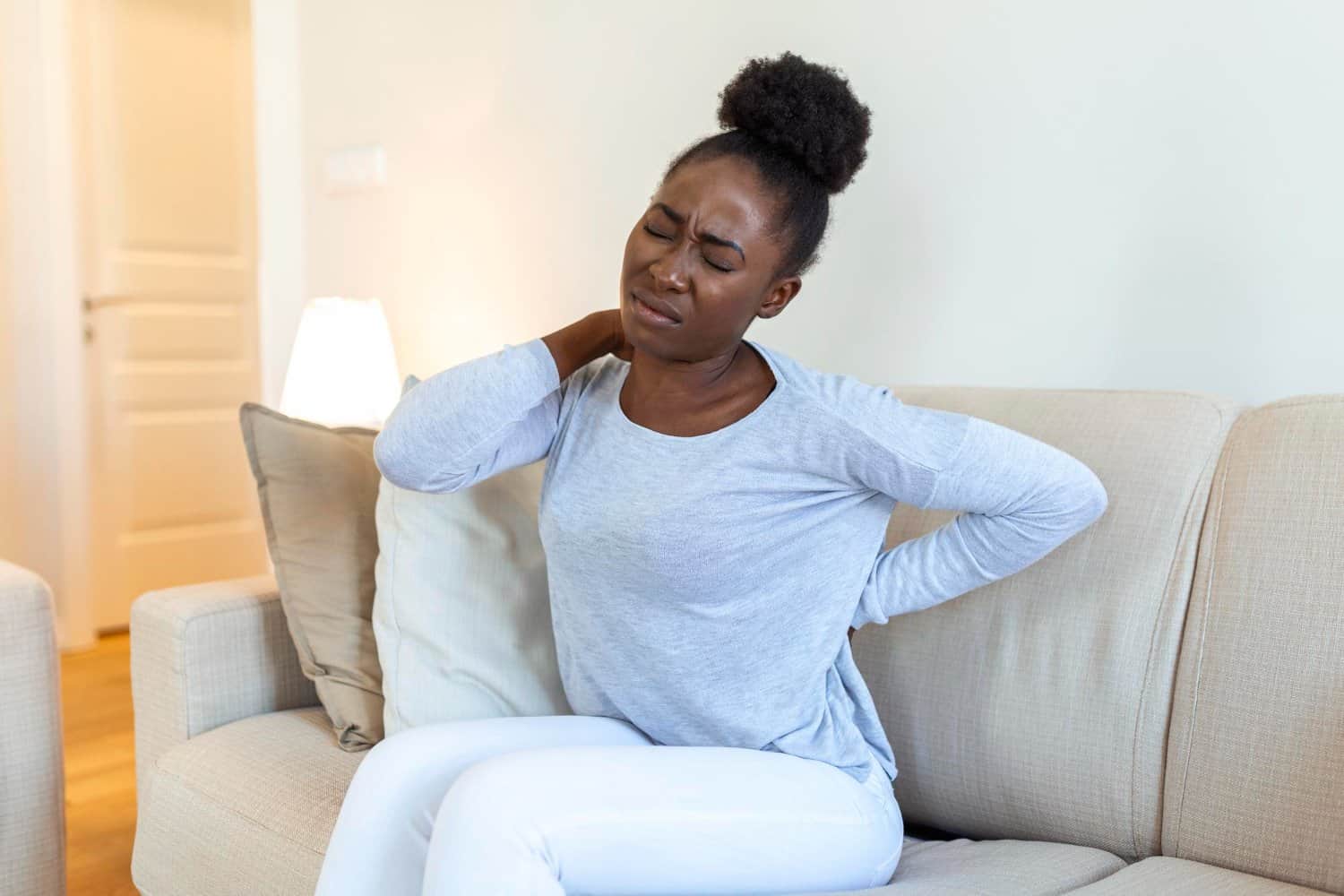 Woman sitting on a couch experiencing physical discomfort and tension in her back